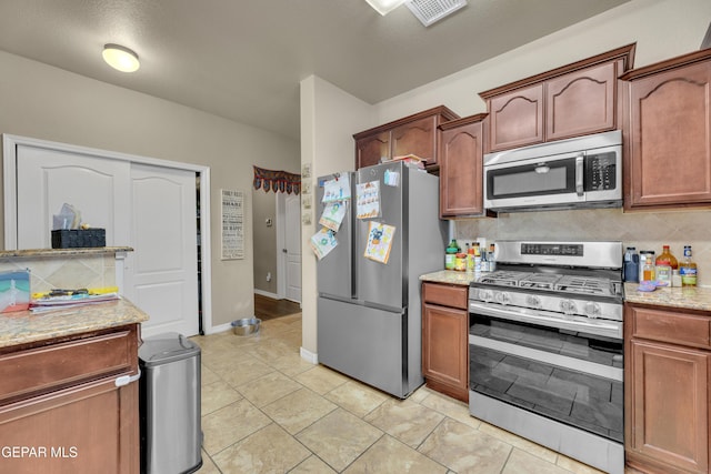 kitchen with light tile patterned floors, stainless steel appliances, decorative backsplash, a textured ceiling, and light stone counters