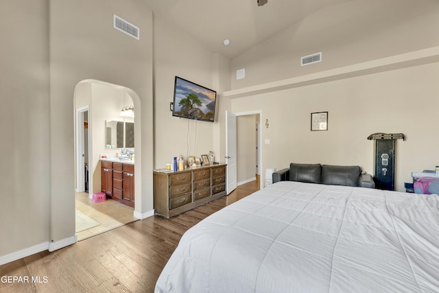 bedroom with high vaulted ceiling, connected bathroom, and light hardwood / wood-style floors