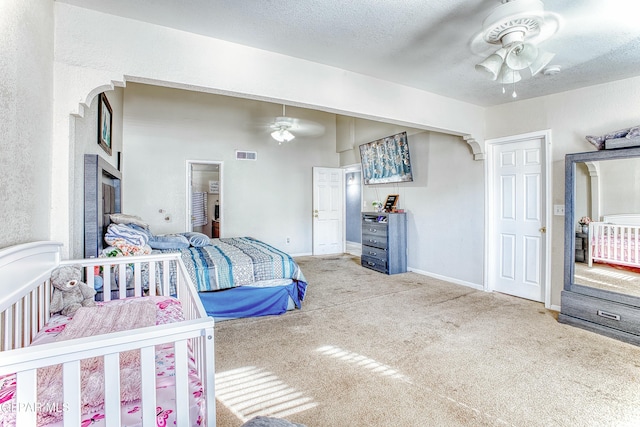 carpeted bedroom with a textured ceiling, a ceiling fan, visible vents, and baseboards