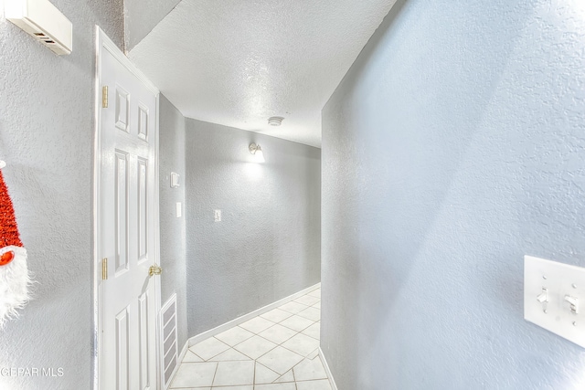 hallway featuring a textured wall, baseboards, a textured ceiling, and light tile patterned flooring