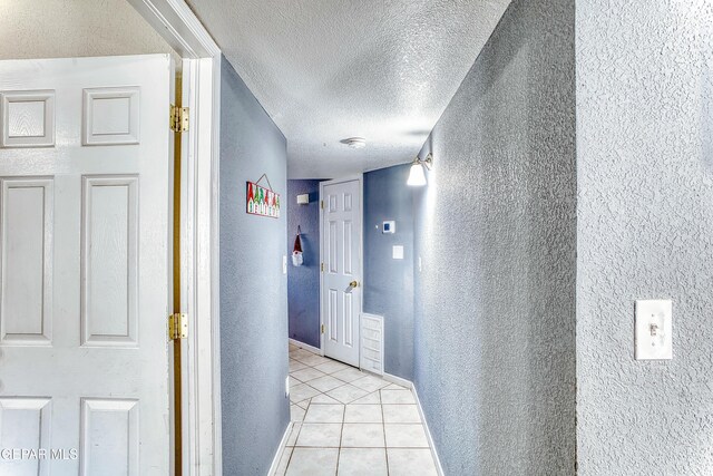 corridor with light tile patterned floors, baseboards, a textured ceiling, and a textured wall