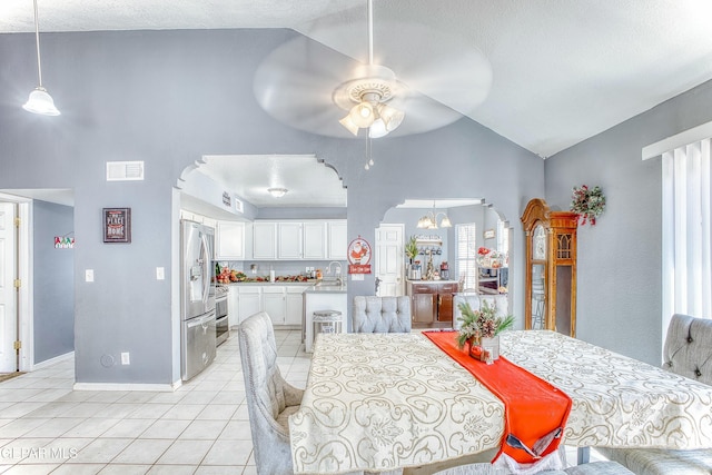 dining room featuring arched walkways, light tile patterned flooring, ceiling fan with notable chandelier, visible vents, and vaulted ceiling