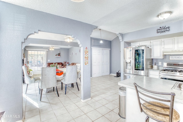 dining room featuring arched walkways, light tile patterned floors, a textured wall, a ceiling fan, and a textured ceiling