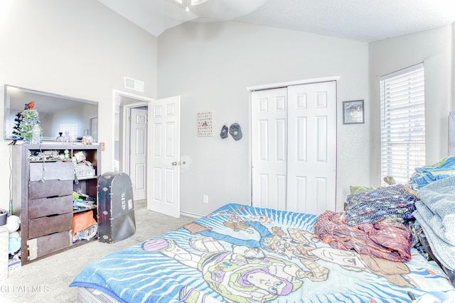 carpeted bedroom with lofted ceiling, a closet, a textured ceiling, and visible vents