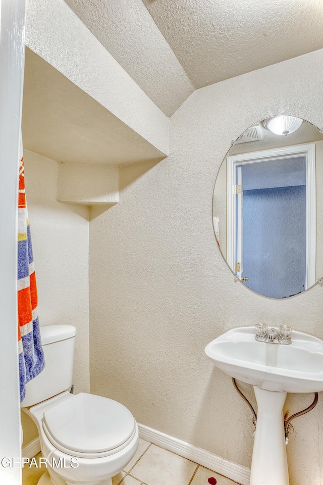 bathroom featuring a textured wall, toilet, a textured ceiling, tile patterned flooring, and baseboards