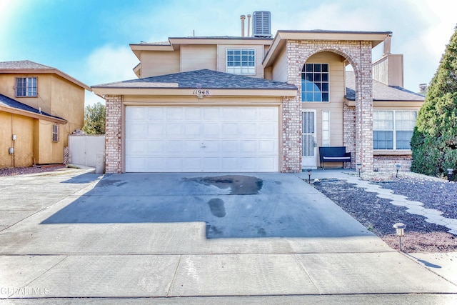 traditional home with central AC unit, a garage, brick siding, a shingled roof, and driveway