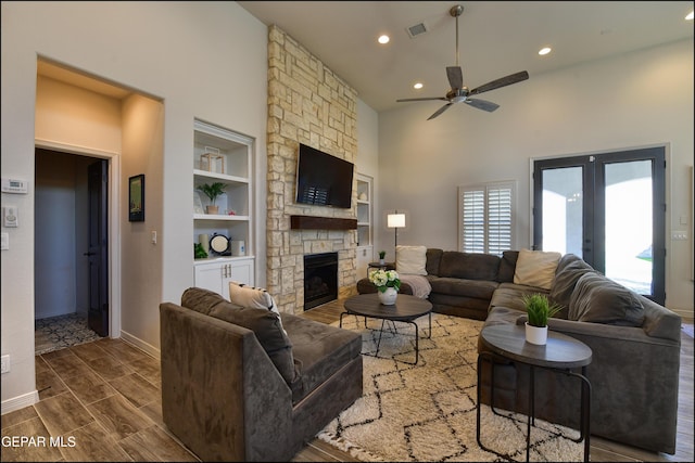 living room with ceiling fan, french doors, a high ceiling, a stone fireplace, and built in features