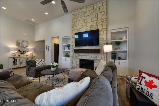 living room featuring ceiling fan, a stone fireplace, wood-type flooring, and built in features