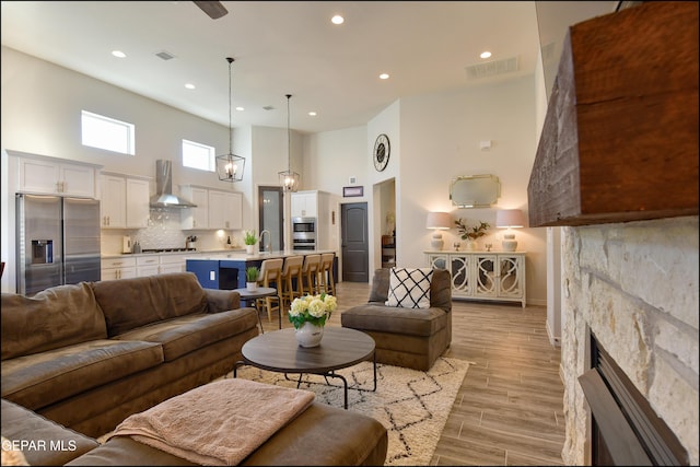 living room featuring a fireplace, a towering ceiling, light hardwood / wood-style floors, and sink