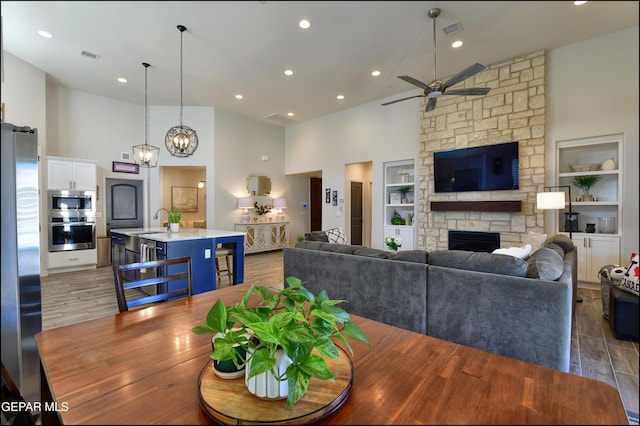 living room featuring ceiling fan, light hardwood / wood-style flooring, built in features, a fireplace, and a high ceiling