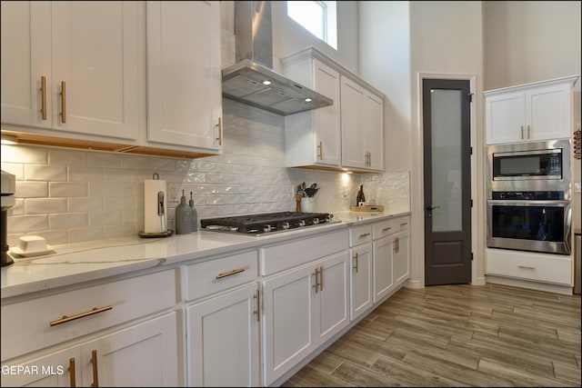 kitchen featuring white cabinets, appliances with stainless steel finishes, light stone countertops, and wall chimney exhaust hood