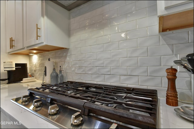 interior details with backsplash, white cabinetry, and stainless steel gas cooktop