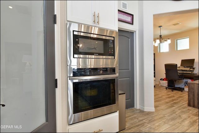 kitchen with multiple ovens, pendant lighting, light hardwood / wood-style flooring, an inviting chandelier, and white cabinets