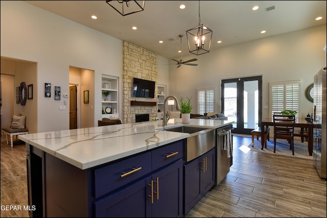 kitchen featuring sink, built in features, stainless steel dishwasher, an island with sink, and ceiling fan with notable chandelier