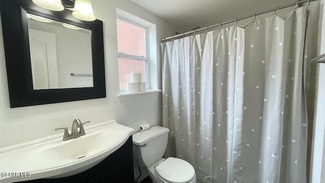 bathroom with a textured ceiling, vanity, toilet, and walk in shower