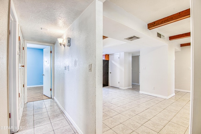 hallway with beam ceiling, light tile patterned floors, and a textured ceiling