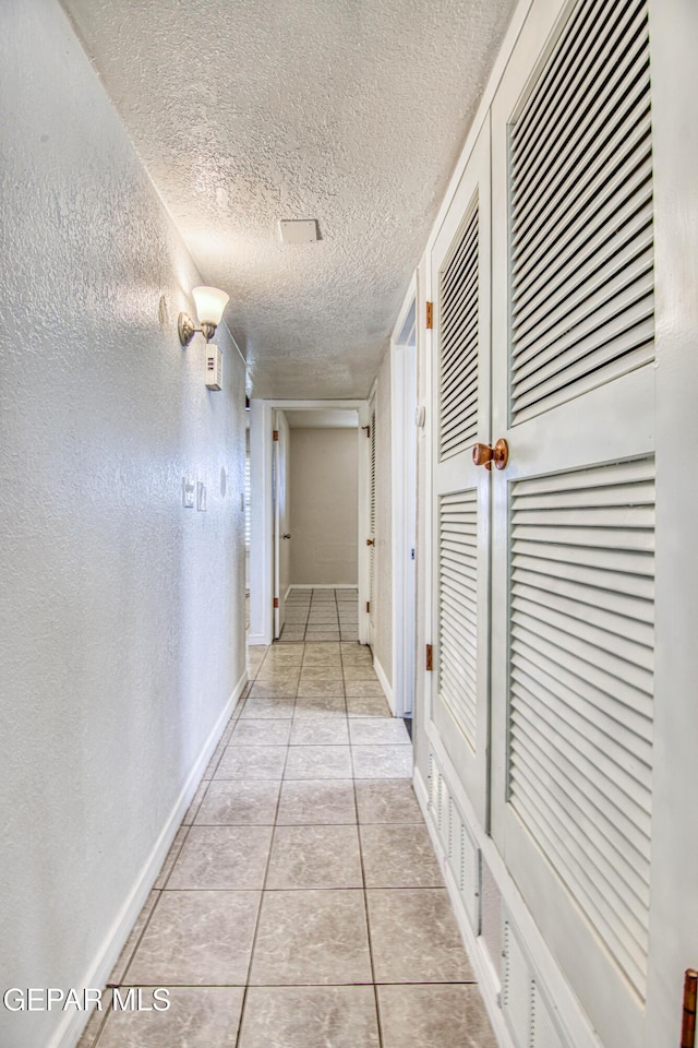 corridor with a textured ceiling and light tile patterned flooring