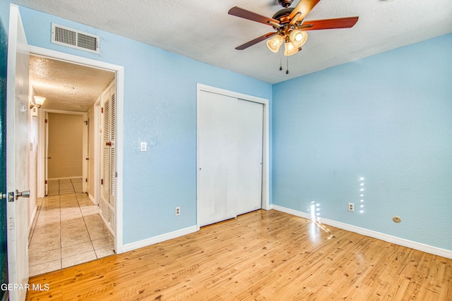 unfurnished bedroom featuring ceiling fan, light hardwood / wood-style floors, a textured ceiling, and a closet