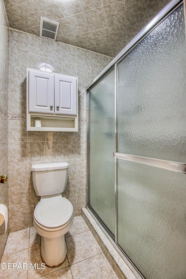 bathroom with tile patterned flooring, toilet, tile walls, and walk in shower