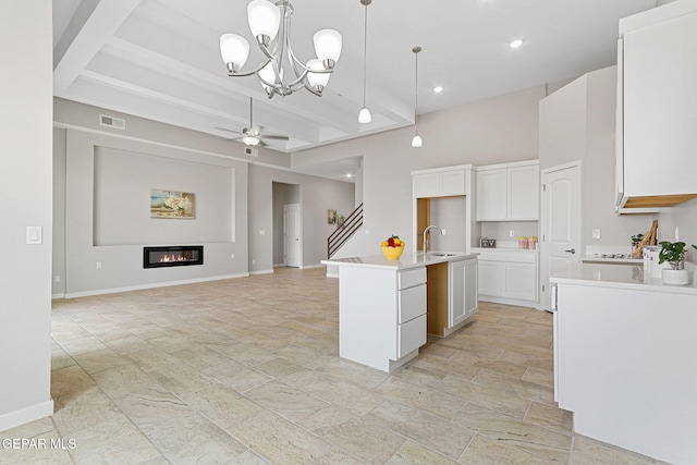 kitchen with pendant lighting, beamed ceiling, white cabinetry, an island with sink, and ceiling fan with notable chandelier