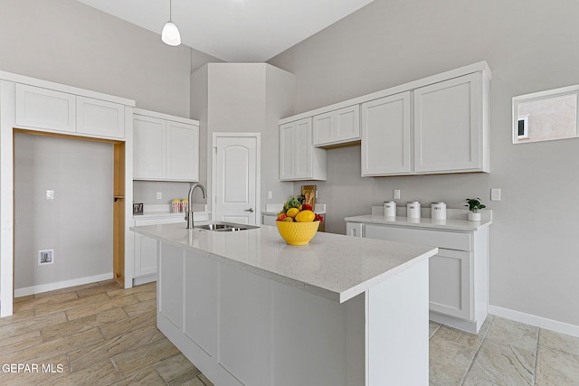 kitchen featuring decorative light fixtures, a kitchen island with sink, white cabinets, and sink