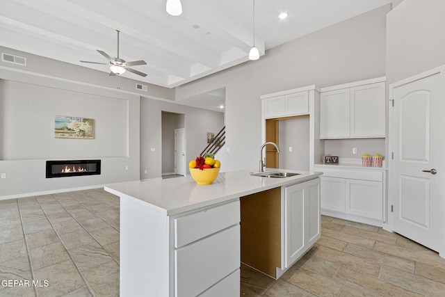 kitchen with pendant lighting, white cabinets, beamed ceiling, sink, and a center island with sink