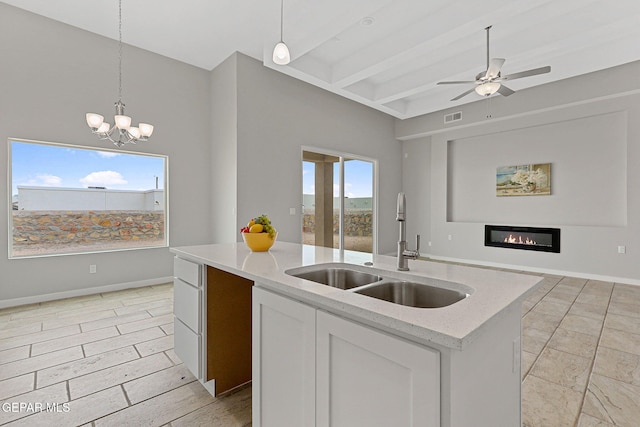 kitchen with sink, hanging light fixtures, a kitchen island with sink, light stone countertops, and white cabinets