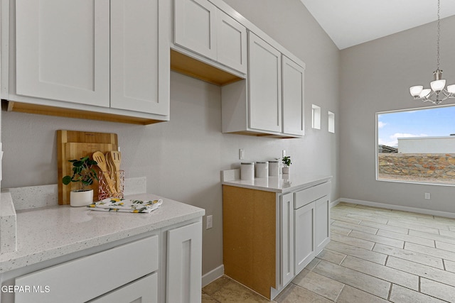 kitchen featuring decorative light fixtures, white cabinets, light stone counters, and an inviting chandelier