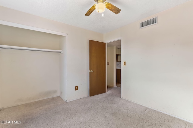 unfurnished bedroom featuring a textured ceiling, ceiling fan, light carpet, and a closet