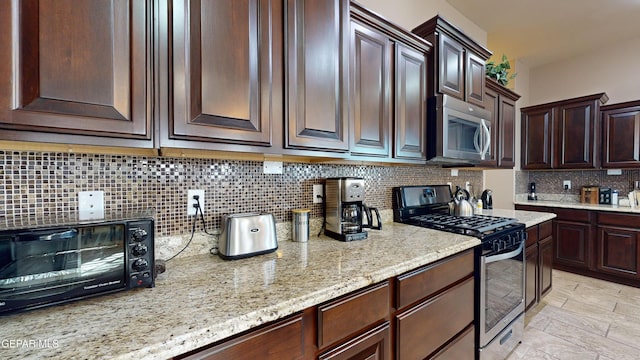 kitchen with dark brown cabinetry, decorative backsplash, stainless steel appliances, and light stone counters