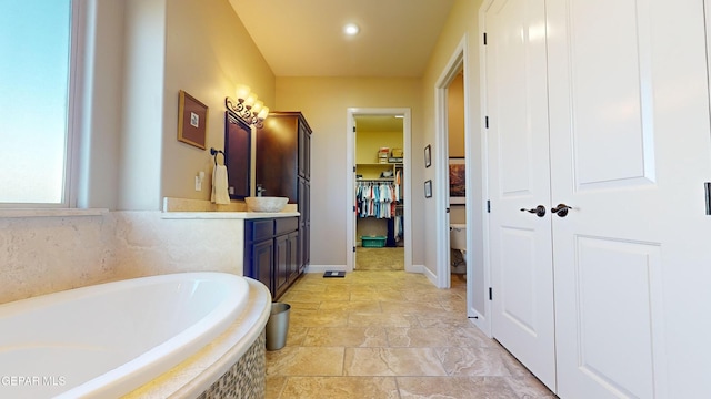 bathroom with tiled tub, vanity, and toilet