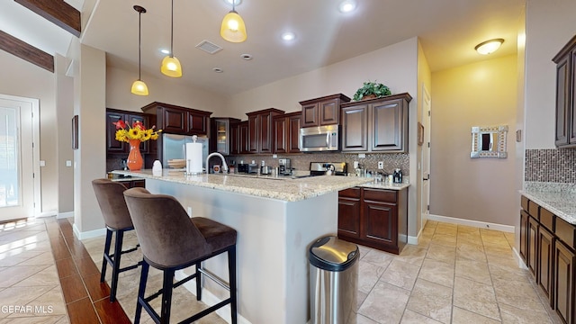 kitchen featuring tasteful backsplash, decorative light fixtures, a kitchen island with sink, light tile patterned floors, and appliances with stainless steel finishes