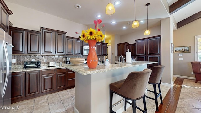 kitchen with hanging light fixtures, decorative backsplash, an island with sink, appliances with stainless steel finishes, and light stone counters