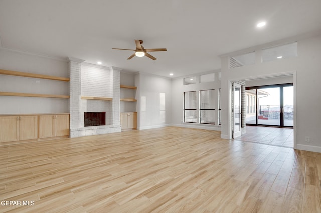 unfurnished living room featuring ceiling fan, light wood-type flooring, a fireplace, and built in shelves