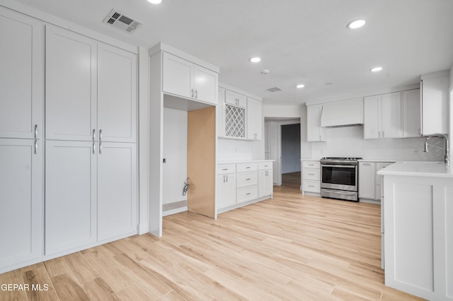 kitchen featuring stainless steel range, custom range hood, sink, light hardwood / wood-style floors, and white cabinetry