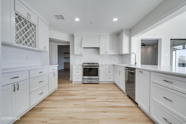 kitchen with premium range hood, decorative backsplash, light hardwood / wood-style floors, white cabinetry, and stainless steel appliances