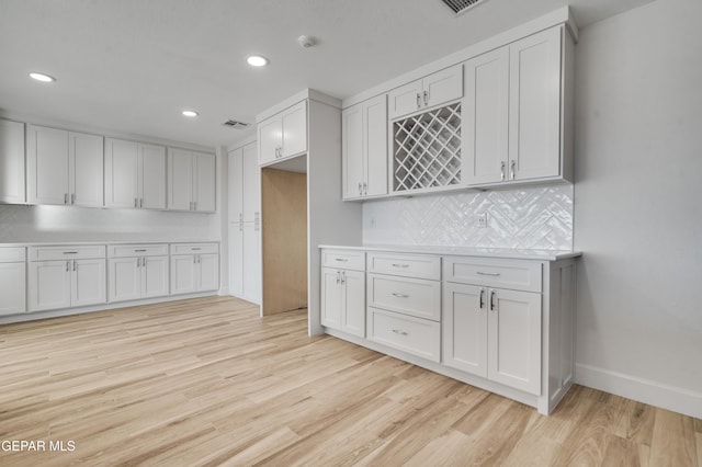 kitchen with white cabinets, light hardwood / wood-style floors, and tasteful backsplash