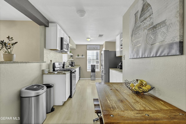 kitchen with white cabinets, appliances with stainless steel finishes, and light hardwood / wood-style flooring