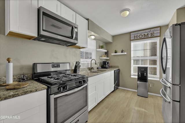 kitchen with light wood-type flooring, stainless steel appliances, sink, dark stone countertops, and white cabinets