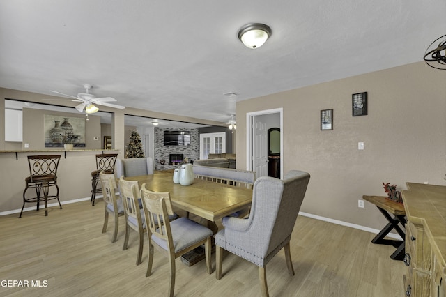 dining room featuring a fireplace, light hardwood / wood-style flooring, and ceiling fan