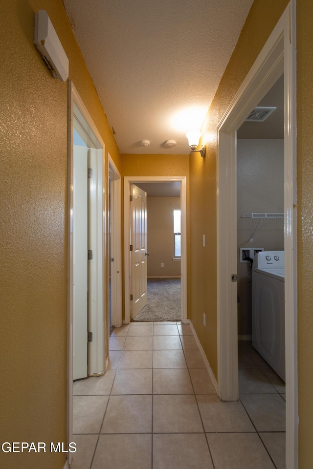 hall featuring light tile patterned flooring, washer / dryer, and a textured ceiling