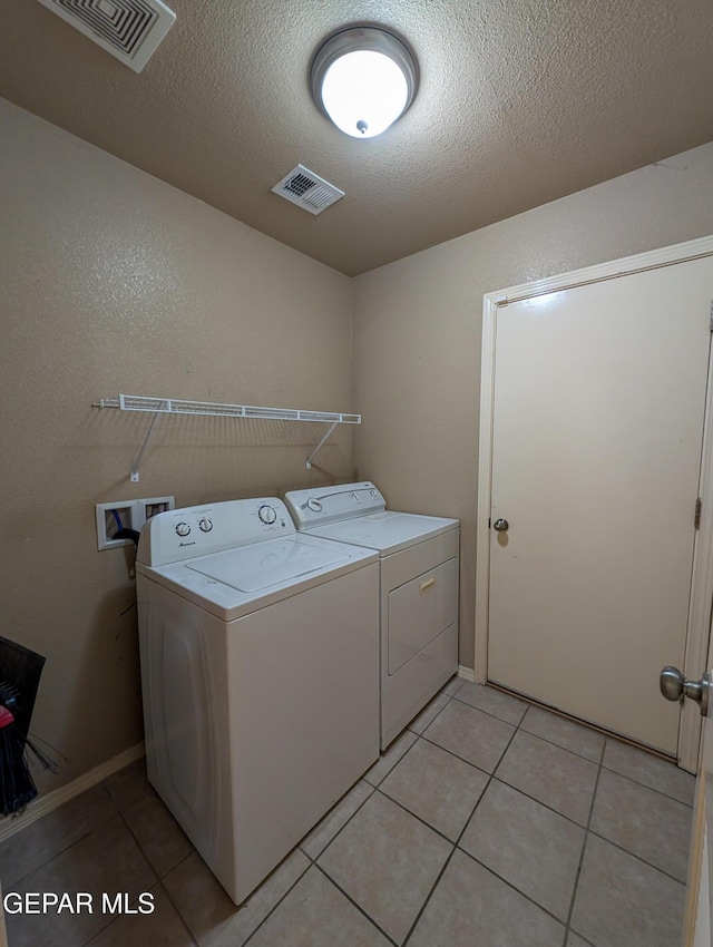 laundry room with washing machine and clothes dryer, light tile patterned flooring, and a textured ceiling