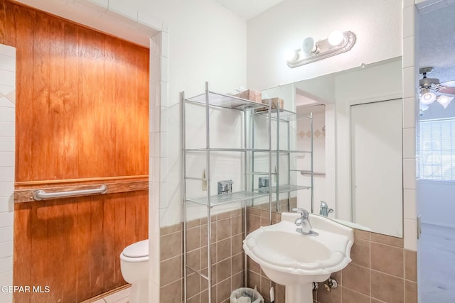 bathroom with tile walls, toilet, ceiling fan, and sink