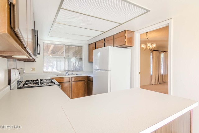 kitchen with kitchen peninsula, white appliances, an inviting chandelier, and sink