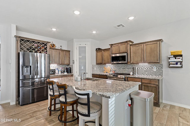 kitchen featuring appliances with stainless steel finishes, a kitchen breakfast bar, light stone counters, sink, and an island with sink