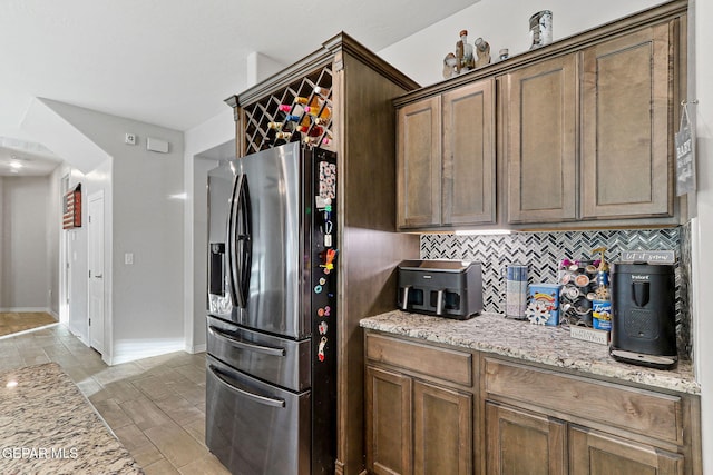 kitchen with decorative backsplash, stainless steel fridge with ice dispenser, and light stone counters