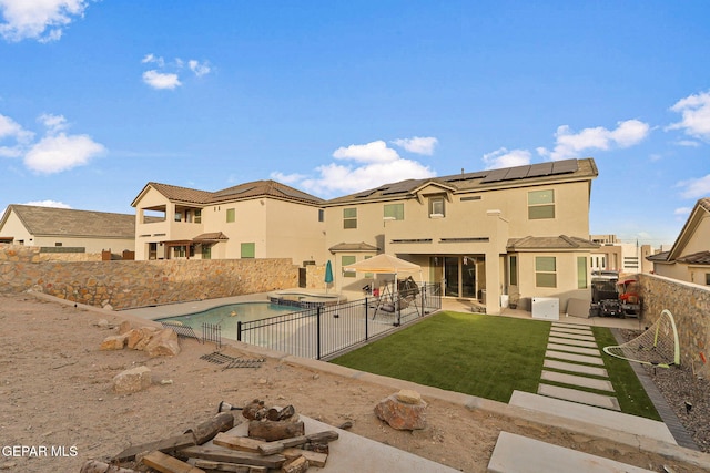 rear view of house featuring solar panels, a fenced in pool, a yard, and a patio