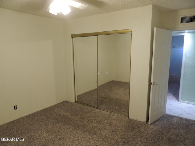 unfurnished bedroom with light carpet, a textured ceiling, a closet, and ceiling fan