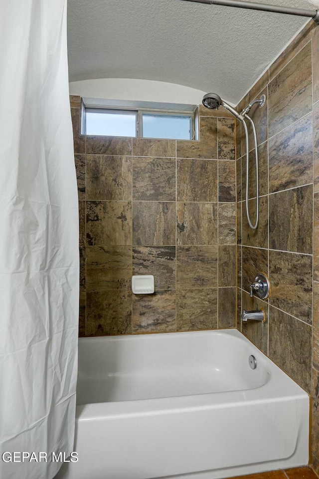 bathroom with shower / bathtub combination with curtain and a textured ceiling