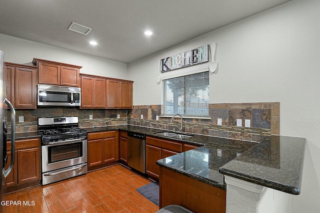 kitchen featuring sink, tasteful backsplash, dark stone countertops, kitchen peninsula, and appliances with stainless steel finishes